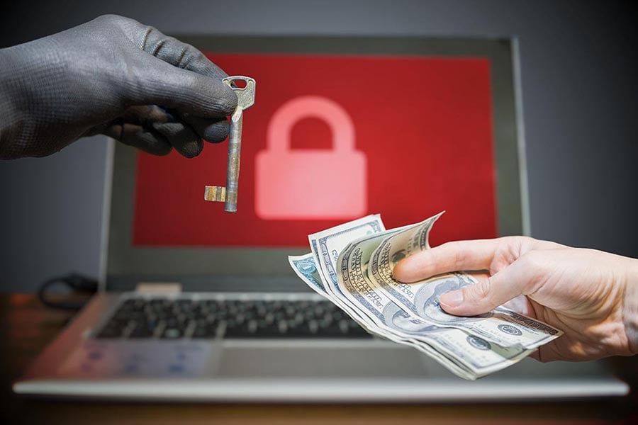 Symbolfoto für eine Erpressung nach einem Ransomangriff. Es ist eine Hand mit einem Schlüssel und eine andere Hand mit Geldscheinen zu sehen. Im Hintergrund ist ein Bildschirm mit rotem Schloss erkennbar.