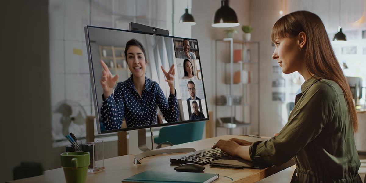 Eine Frau sitzt im Homeoffice an einem Bildschirm, auf dem ein andere Frau zusehen ist. Beide haben eine Videokonferenz. Oben auf dem Bildschirm ist die MeetingBar A10 installiert.