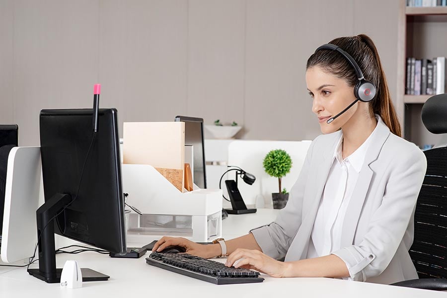 Symbolfoto - Eine junge Frau mit Headset WH62 von Yealink am Computer die mit jemanden spricht - Das Bild soll den Support on Keepsmile Design nach Fertigstellung einer Website zeigen